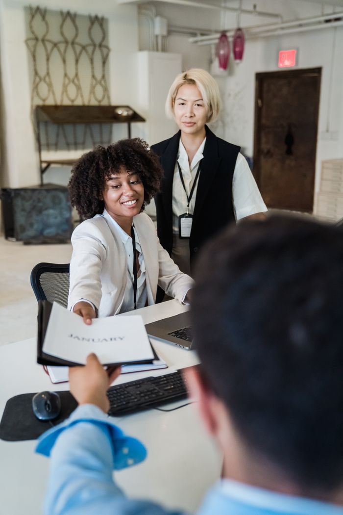 Three diverse colleagues collaborate in a modern office environment, exchanging a document.