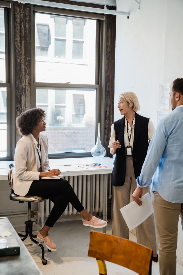 The Art of Drawing Readers In: Your attractive post title goes here Three colleagues engage in a casual meeting in a modern office space, collaborating on a project.