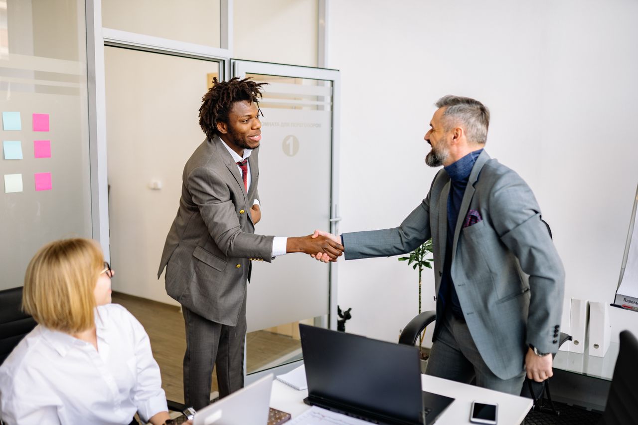 Two businessmen shaking hands in a modern office setting, symbolizing agreement.